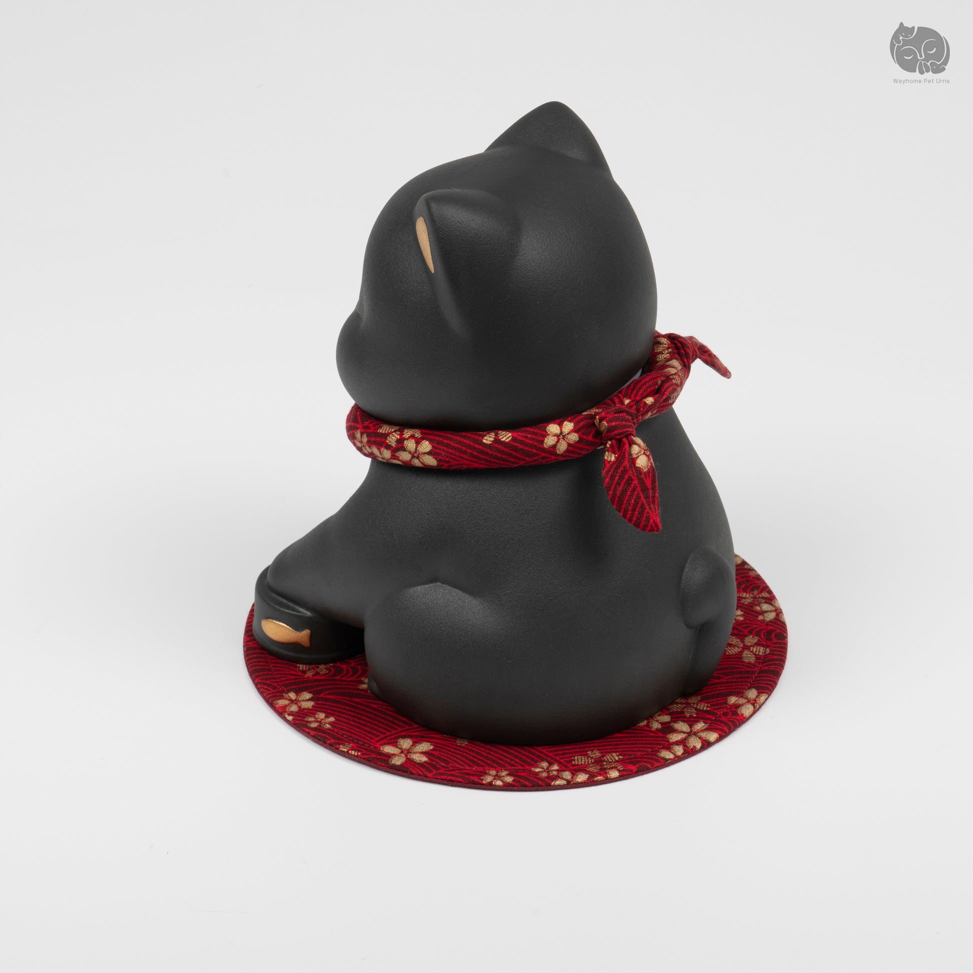 Rear quarter view of the black kitten memorial urn, showing the calm expression and decorative red mat.
