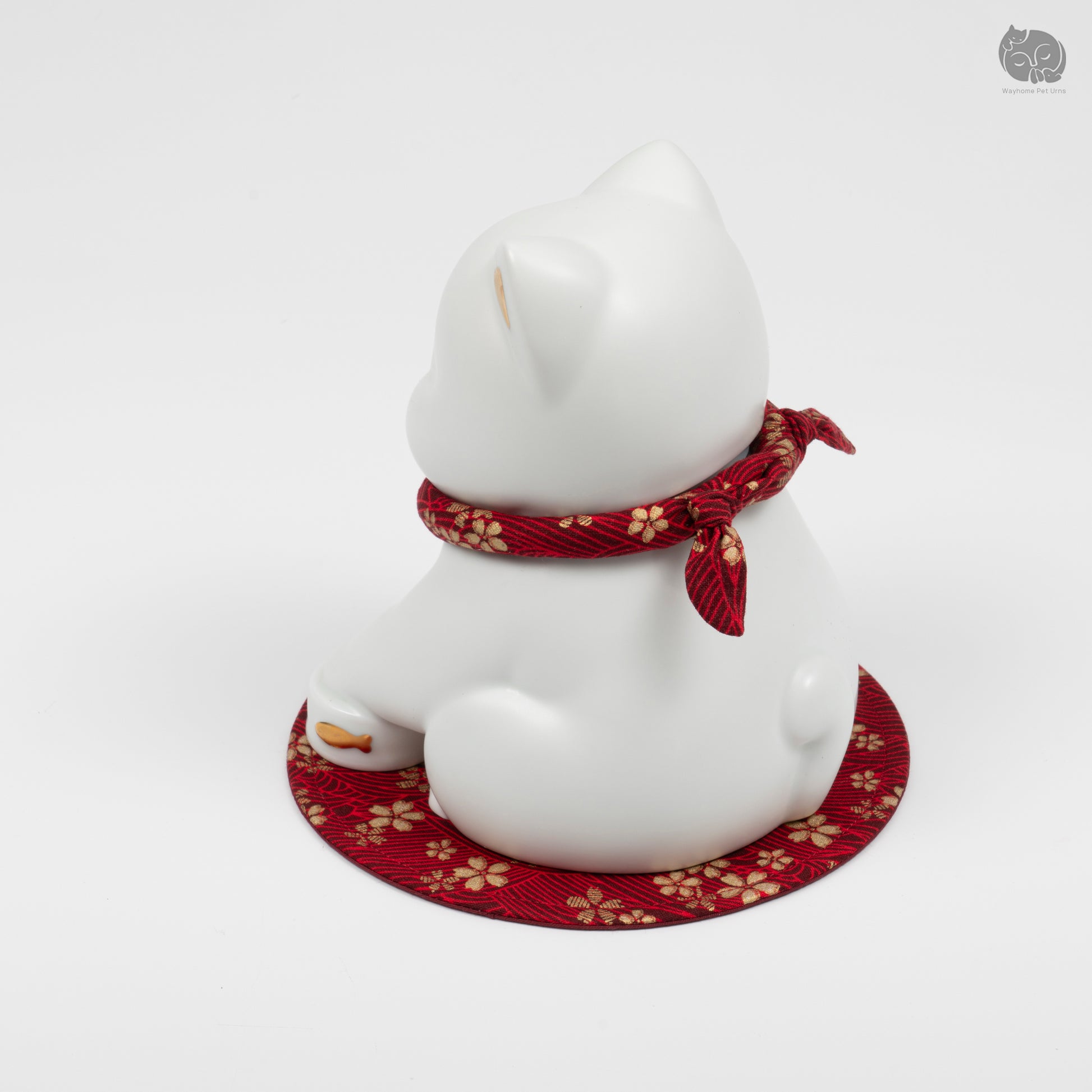 Rear angle view of the white kitten memorial urn, showing the serene expression and decorative red mat.